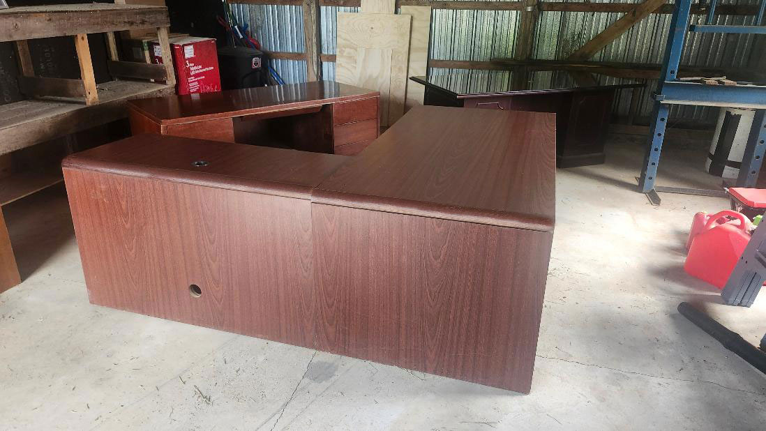 Large L-shaped wood-finish desk in storage